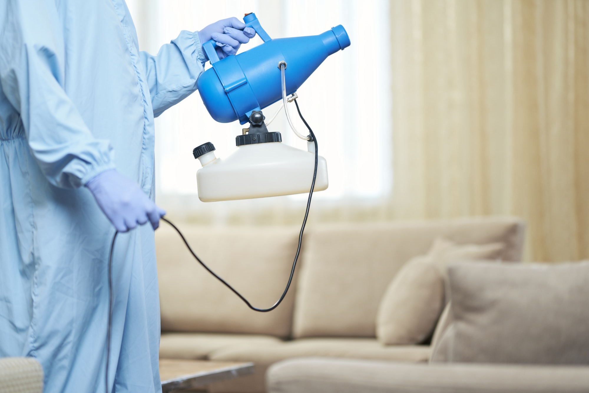 Worker making disinfection in hotel room near sofa